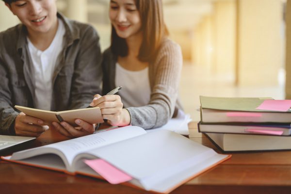 Two students are sitting at table reading books to education. Study for test preparation.